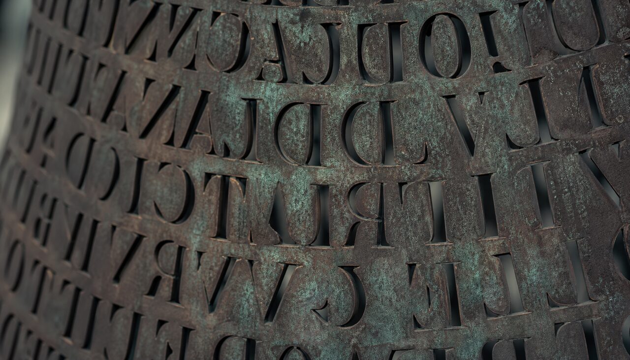 Roughly 1,800 copper letters, cut clean through the panel. Three sections have surrendered. The fourth has not.
